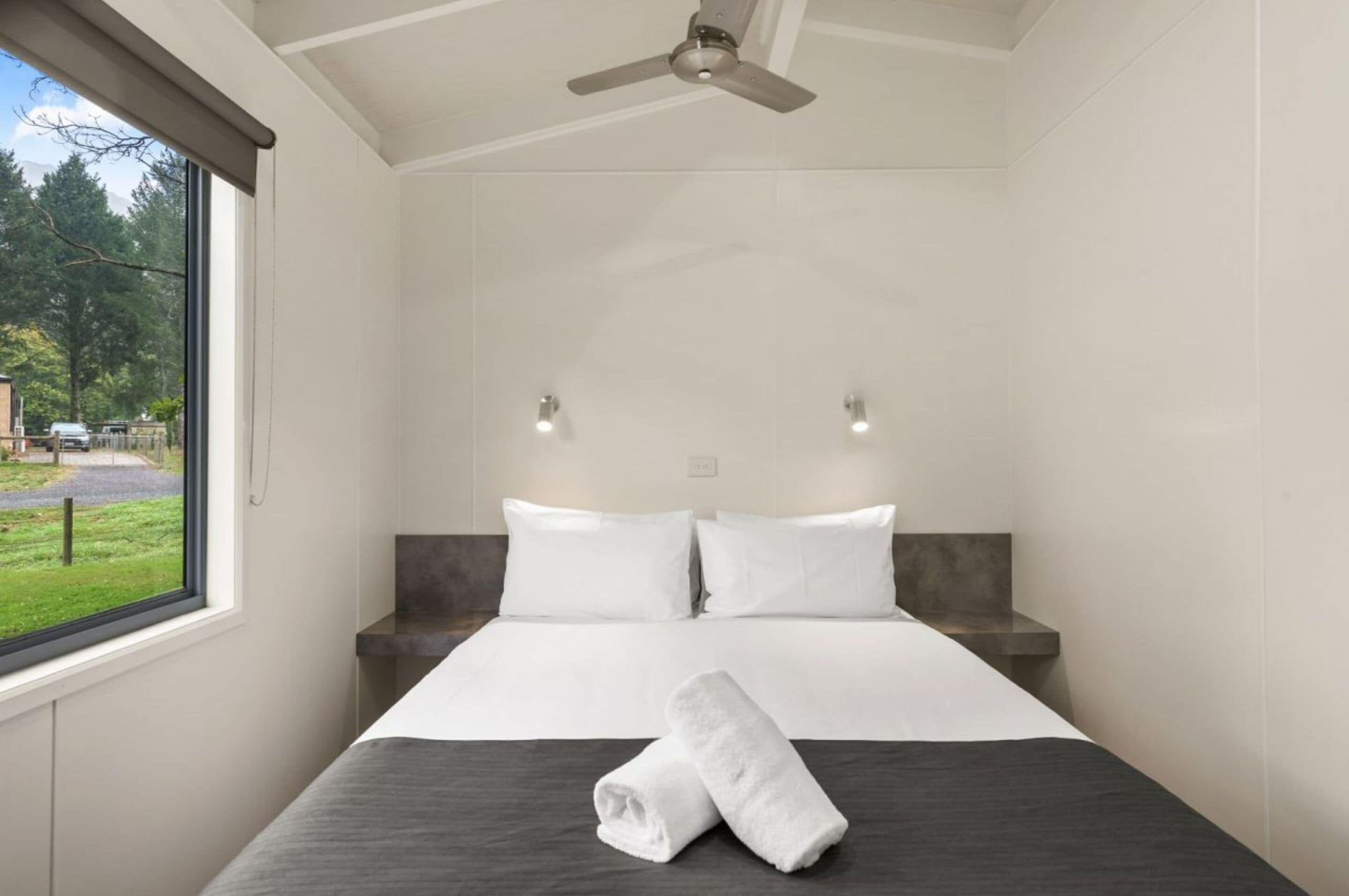 Une chambre d’hôtel avec un grand lit, un ventilateur de plafond et une vue sur l’extérieur par une fenêtre.