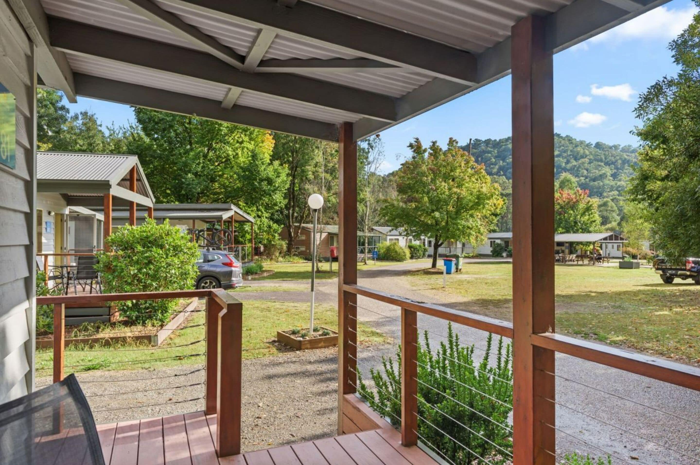 A covered outdoor area with a wooden deck, a view of a residential neighborhood, and a grassy area with trees.