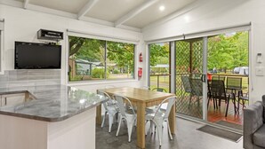 A modern kitchen with a marble countertop, a dining area with a wooden table and chairs, and a sliding glass door leading to an outdoor patio with chairs and a table. - Discovery Parks - Bright (Freeburgh)