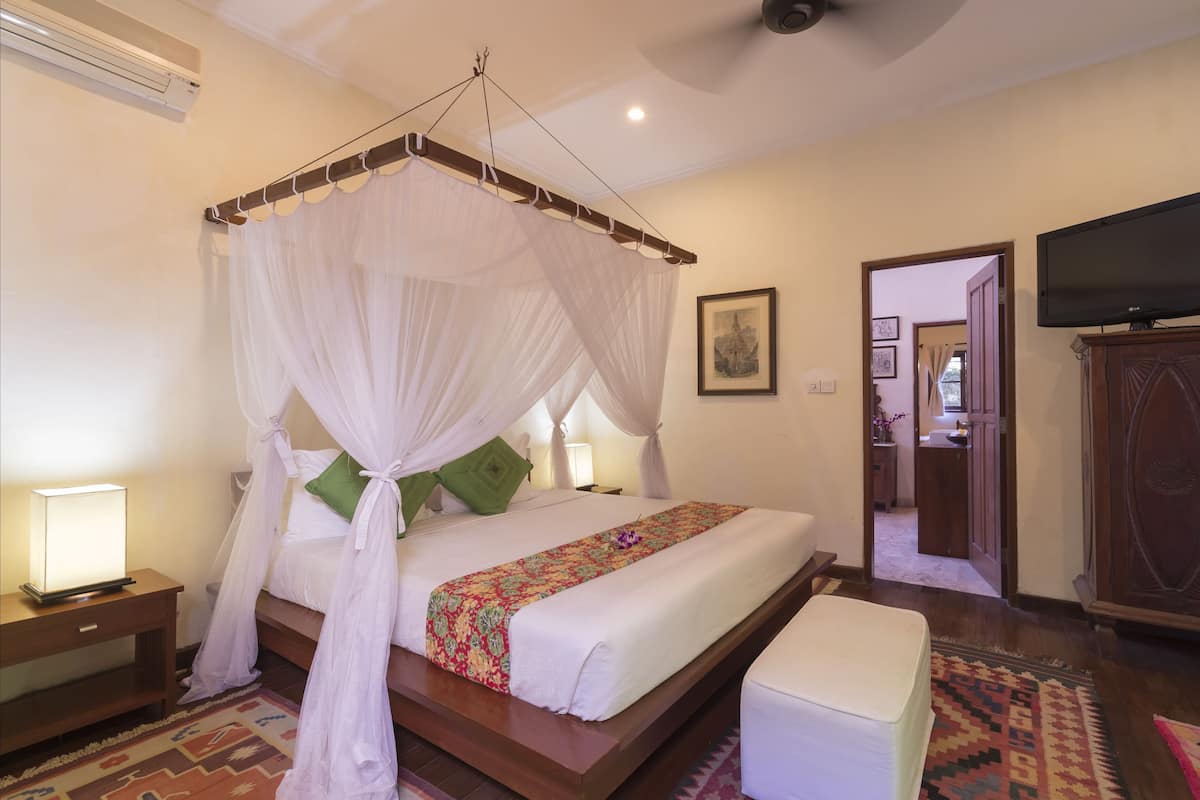 A bedroom with a four-poster bed, a television, and a wooden cabinet.