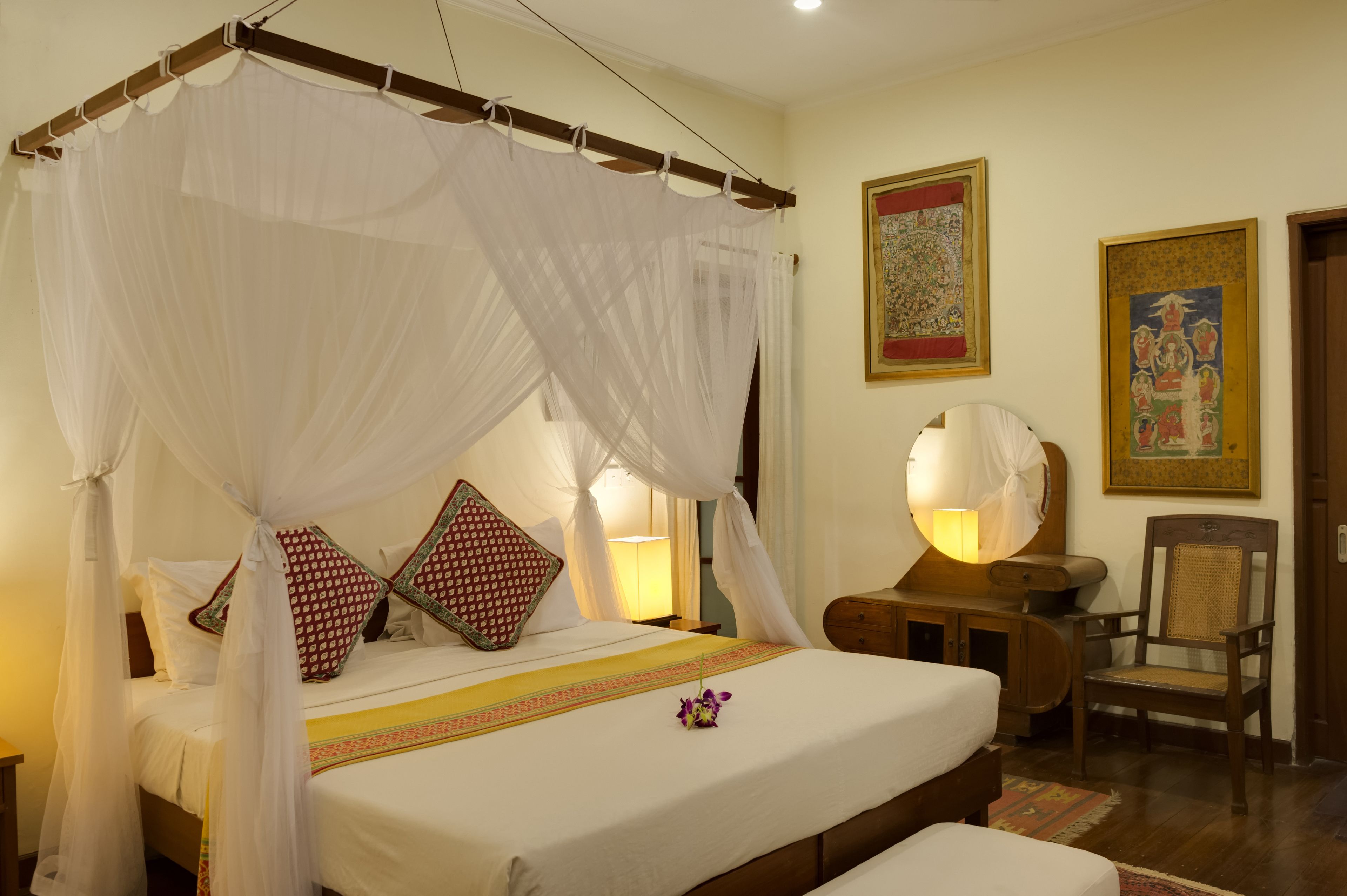 A bed with a canopy, a bedside lamp, a chair, and a wall with a framed picture.