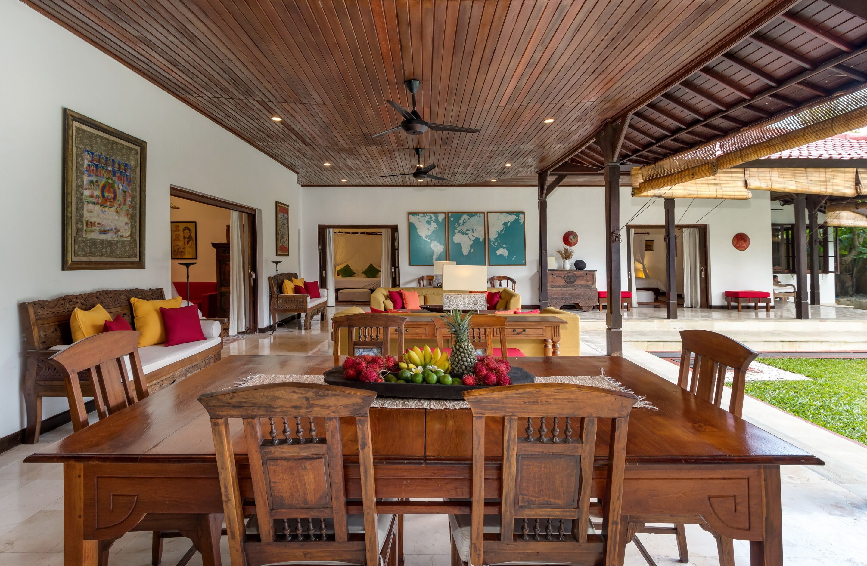 Un comedor amplio con una mesa y sillas de madera, un centro de mesa con frutas y un ventilador de techo.