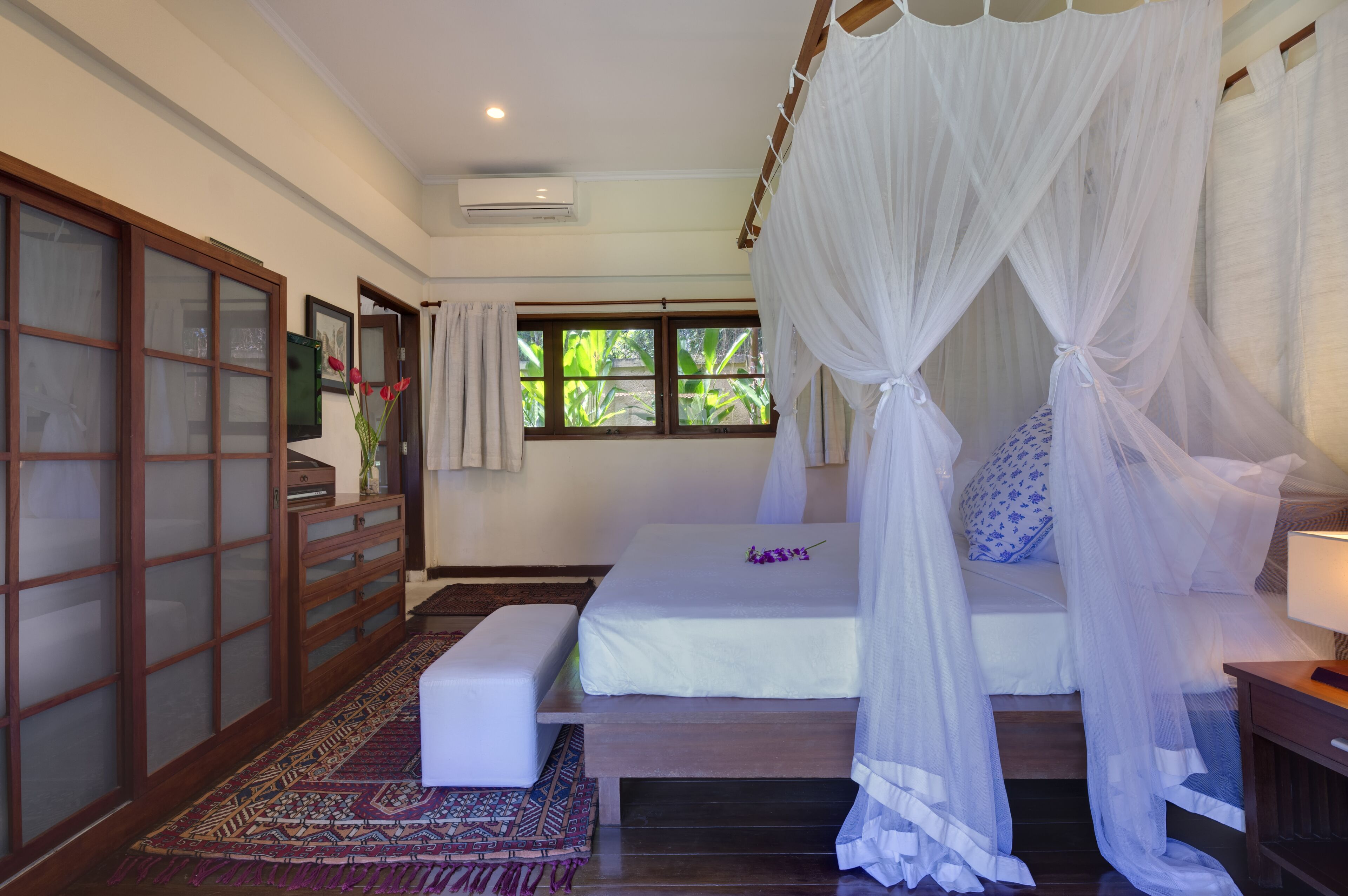 A bedroom with a canopy bed, a wooden wardrobe, and a patterned rug.