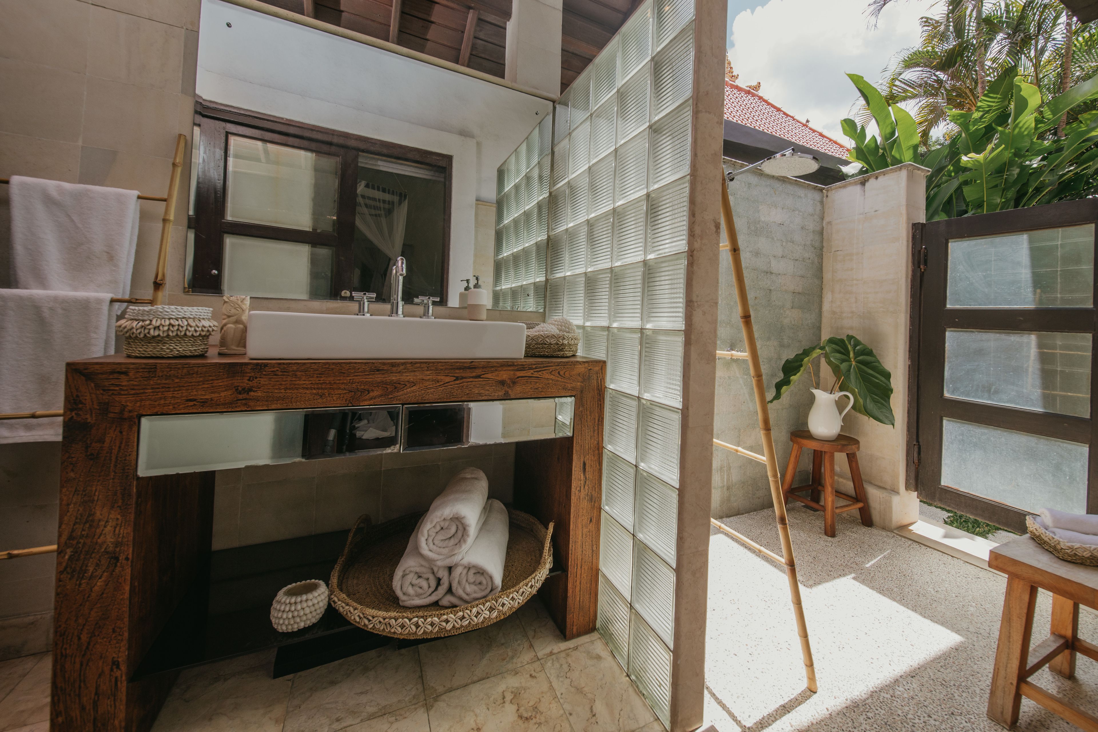 Ein Badezimmer mit einem Holzkosmetikschrank, einem großen Spiegel, einer Badewanne und einem Fenster mit Blick auf Grünflächen.