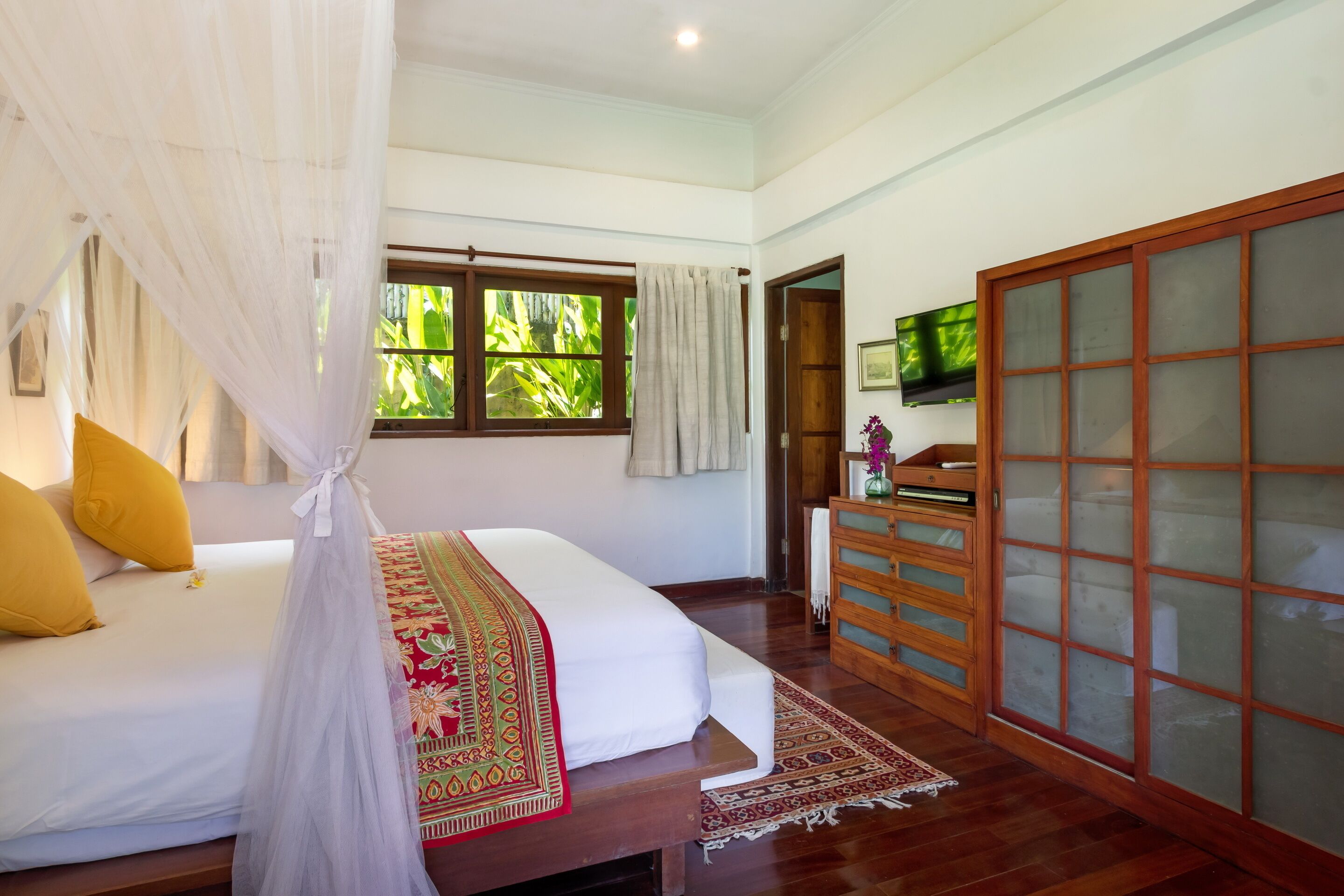 A bedroom with a bed, a wooden dresser, a television, and a window with curtains.