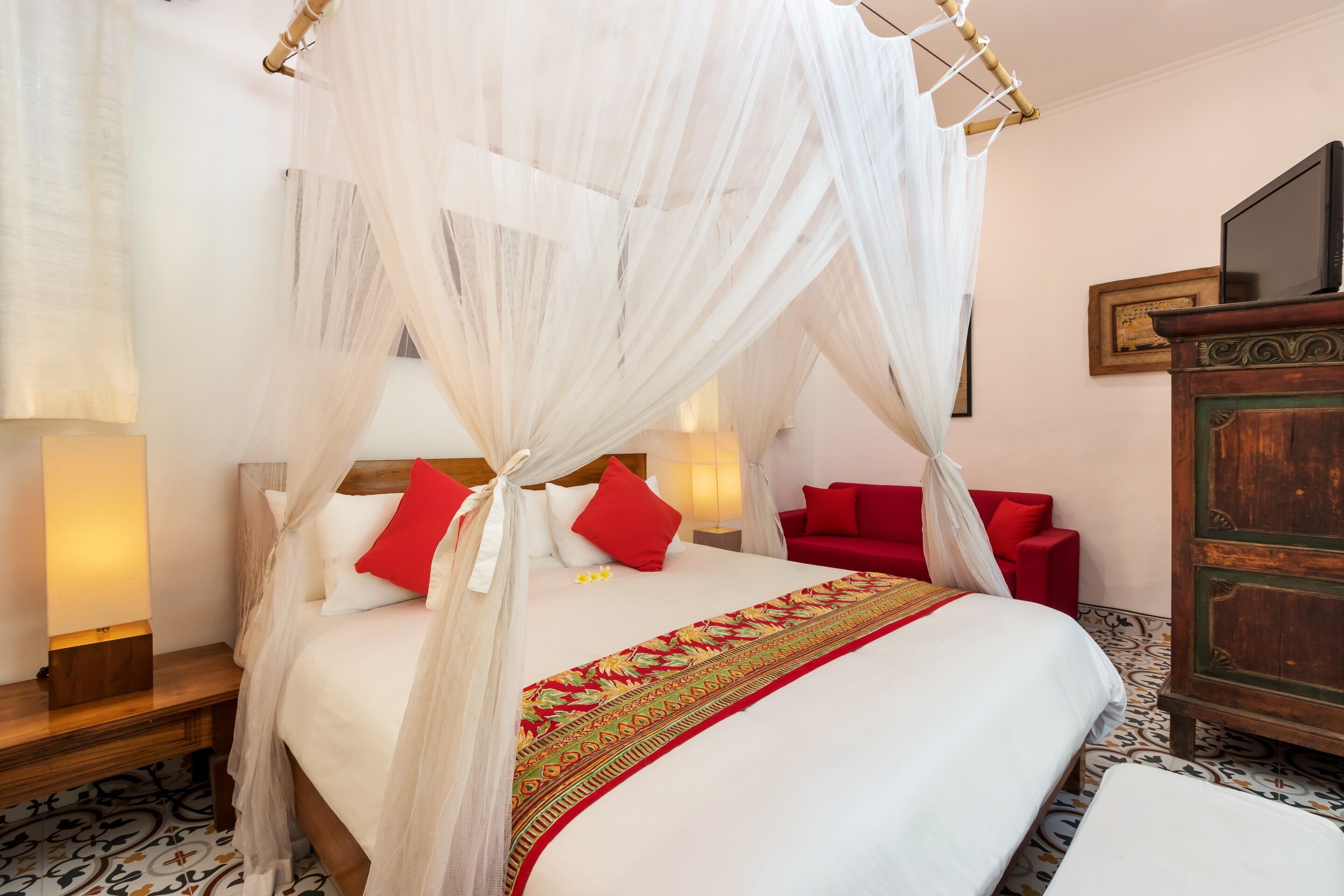 Une chambre à coucher avec un lit à baldaquin, un canapé rouge, une commode en bois et un téléviseur posé sur un meuble en bois.