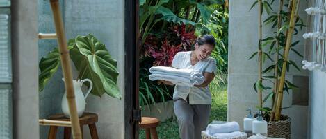 A bathroom with a stone wall, a wooden stool, a table with towels, and a potted plant.