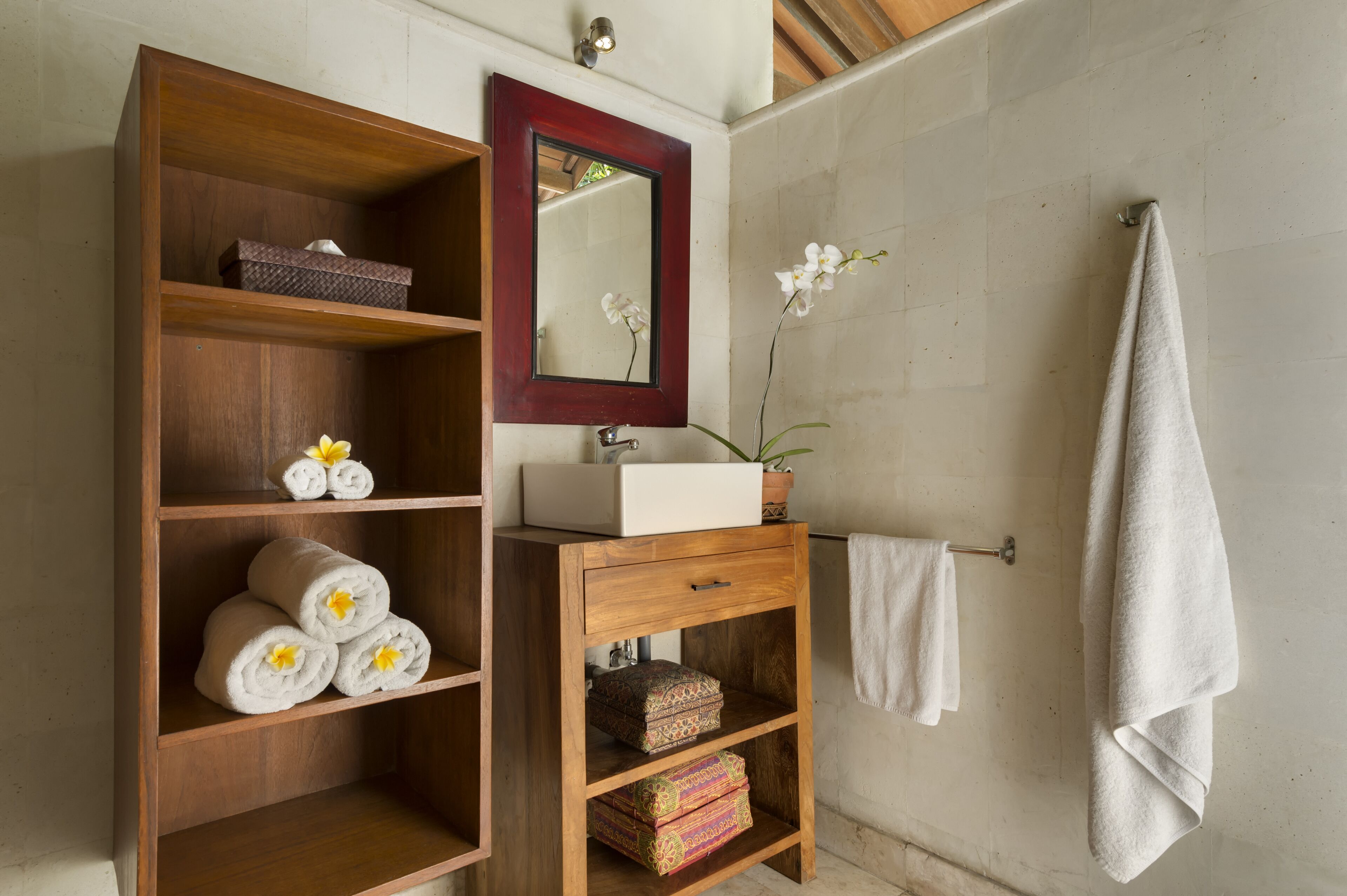 A wooden vanity with a mirror, a sink, and shelves holding towels and decorative items.