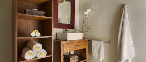 A wooden vanity with a mirror, a sink, and shelves holding towels and decorative items.