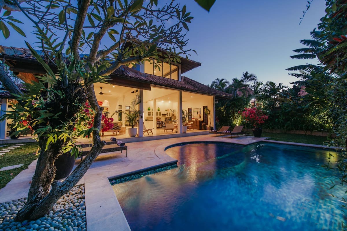 A modern house with a swimming pool, surrounded by lush greenery and tropical plants.