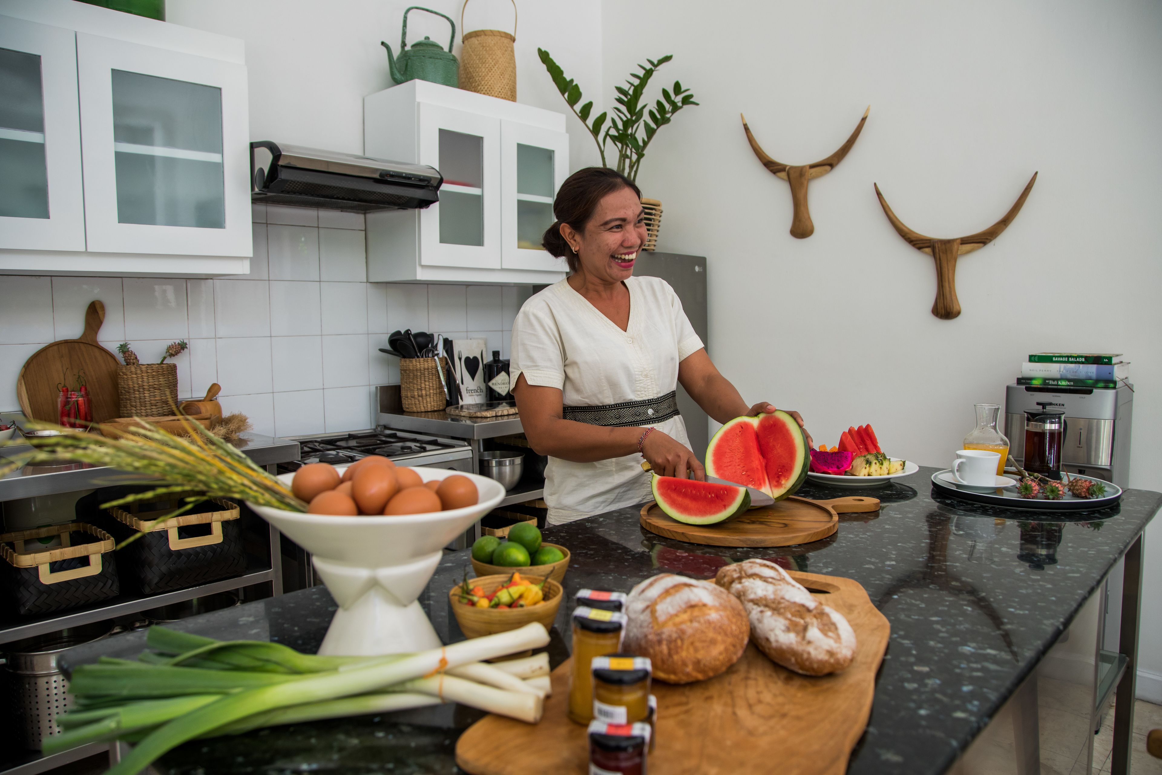 A kitchen with white cabinets, a black countertop, and various food items like eggs, watermelon, and bread.