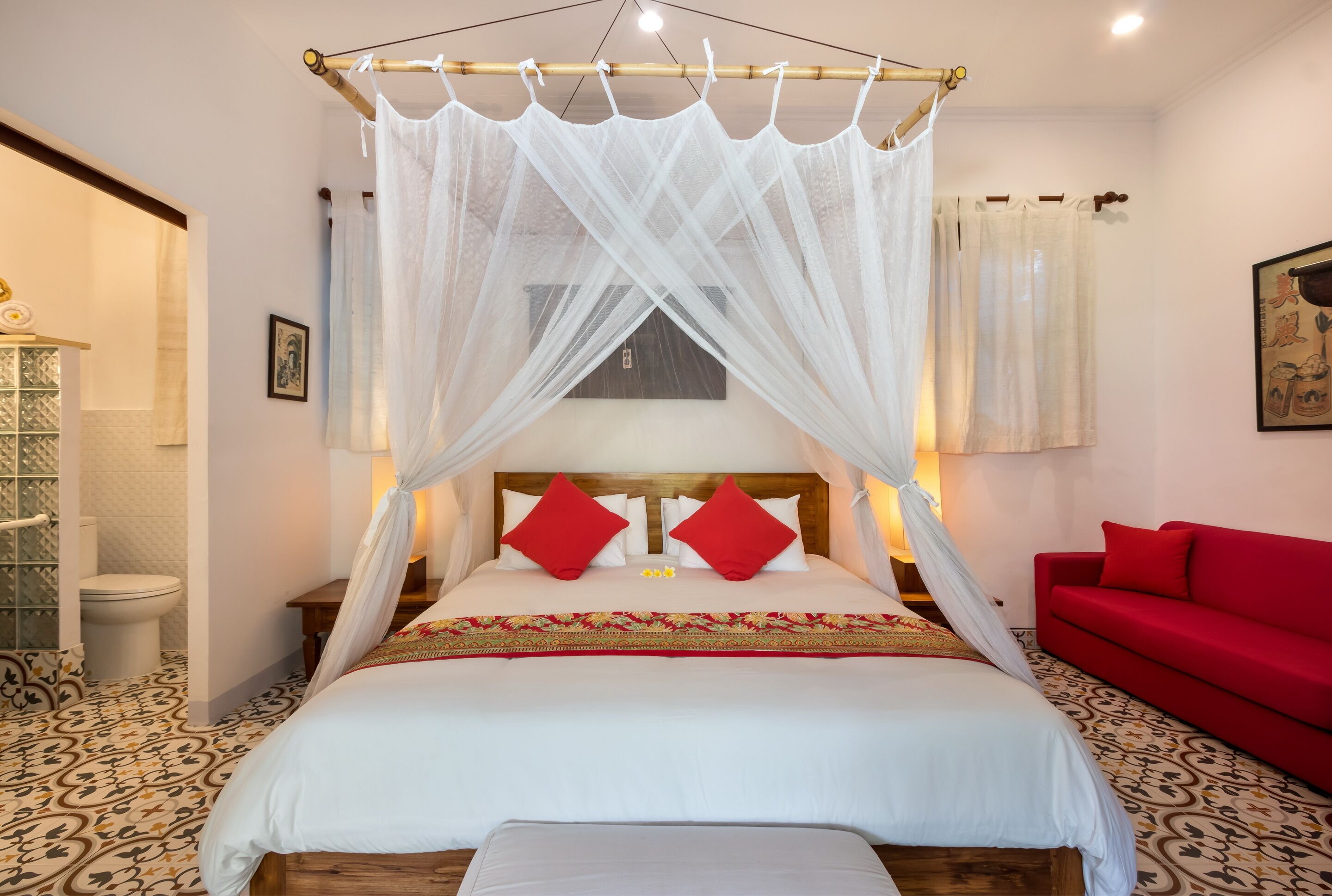 A bedroom with a canopy bed, a red sofa, and a patterned floor.