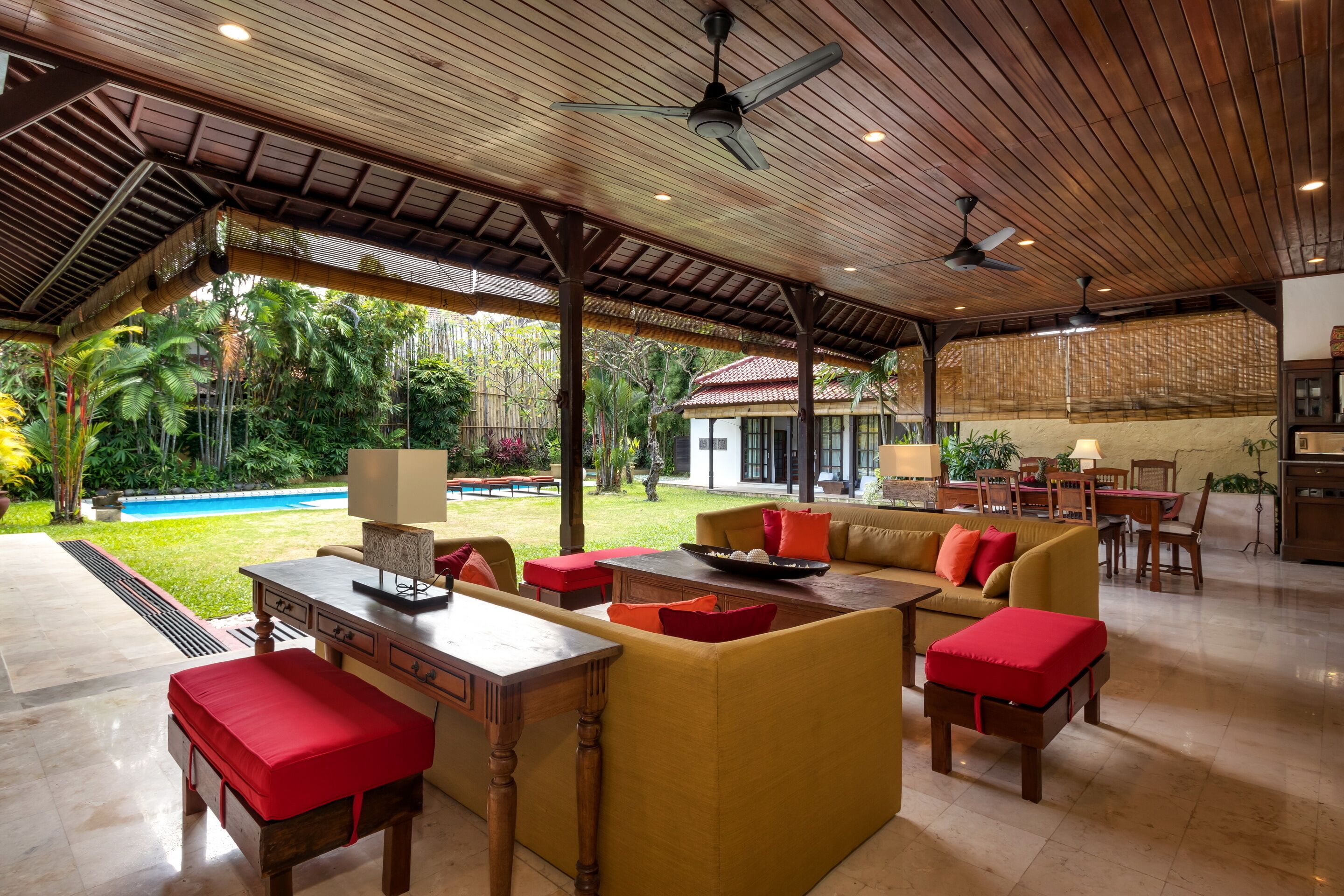 A spacious outdoor living area with a pool, wooden furniture, and a covered seating area.