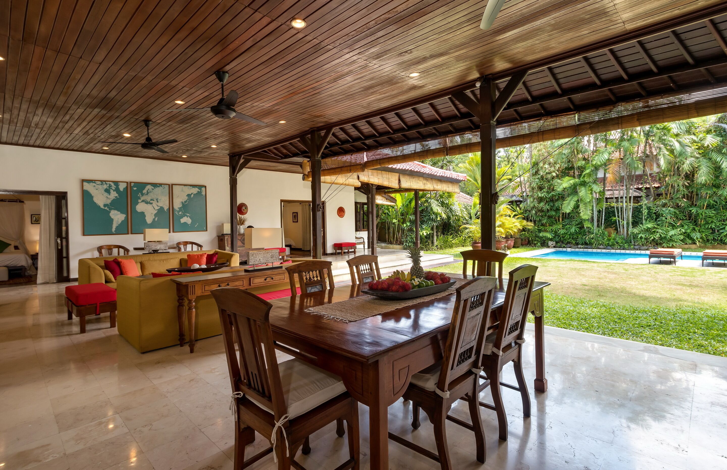 A spacious living area with a wooden ceiling, a dining table set for six, and a view of a swimming pool.
