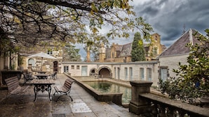 A courtyard with stone benches, a fountain, and a building with arched windows and a clock tower. - Eltham Retreat Guest House (Eltham)