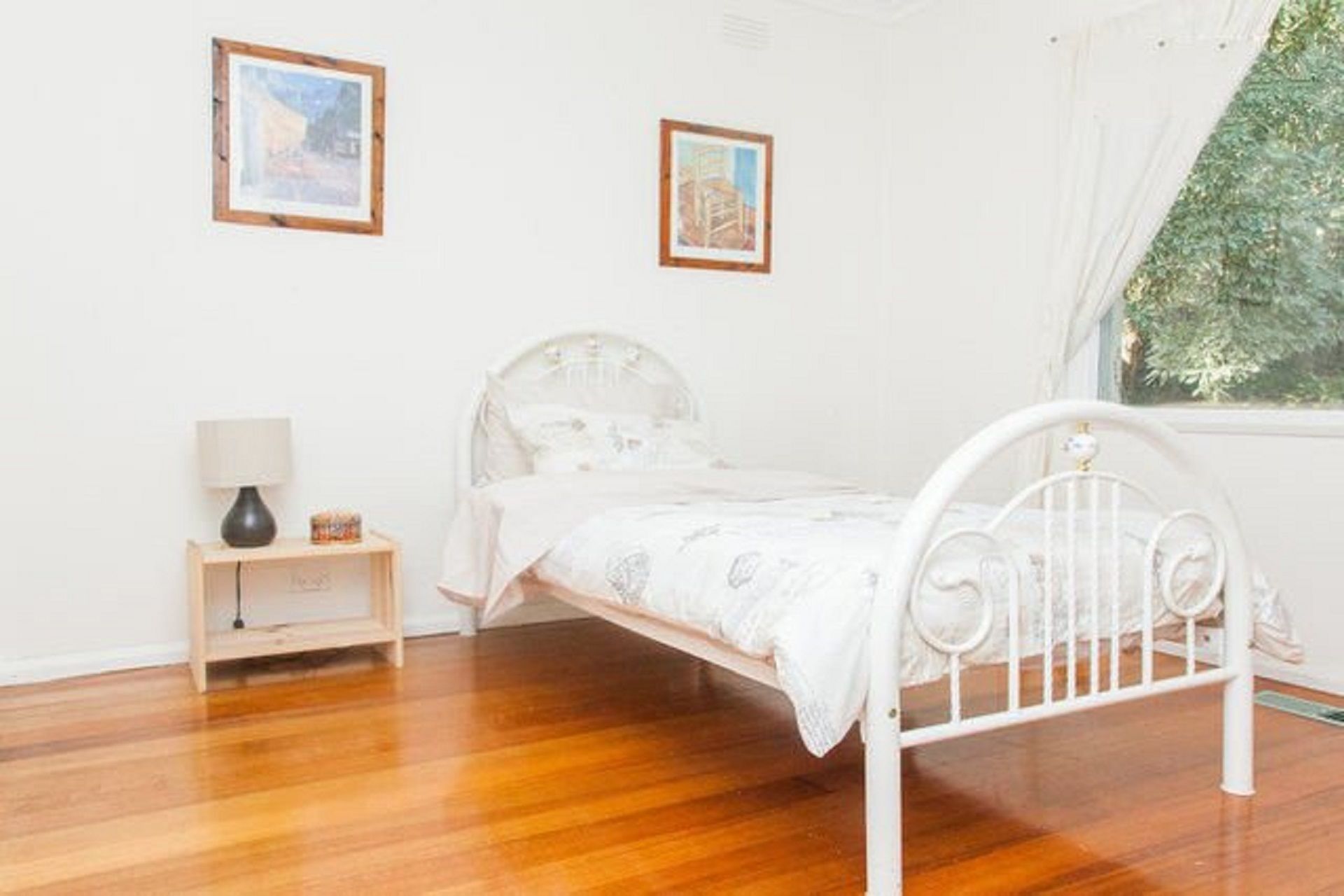 Una camera da letto con un letto in metallo bianco, un comodino con una lampada e due quadri appesi al muro.