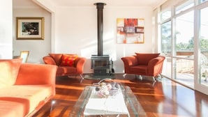 A spacious living room with a large window, a fireplace, two armchairs, and a coffee table. - Eltham Retreat Guest House (Eltham)