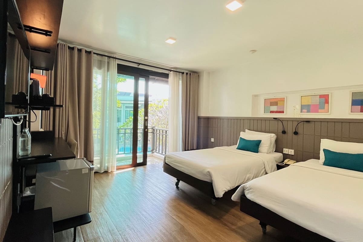Quarto de hotel com duas camas, uma escrivaninha, uma cadeira, uma televisão e varanda com cortinas.