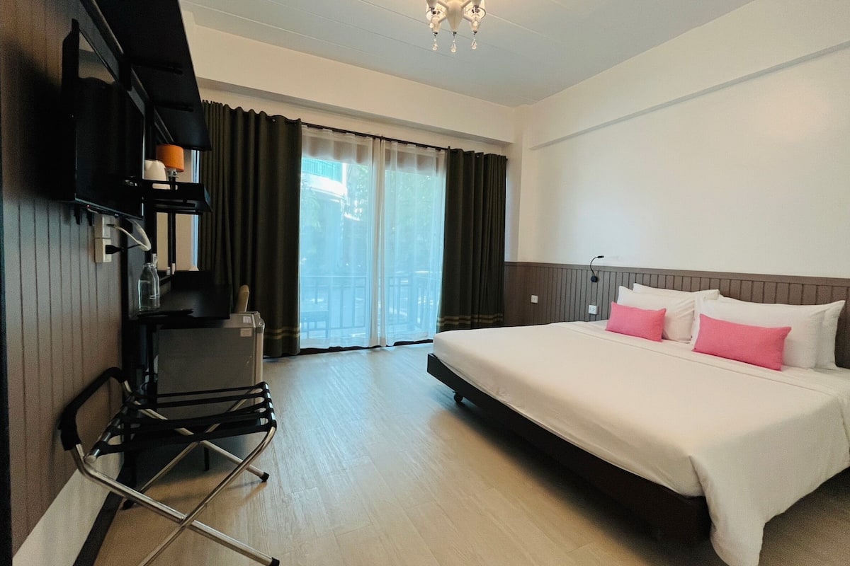 Quarto de hotel com uma cama grande, uma escrivaninha com cadeira, televisão e janela com cortinas.