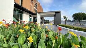 A modern building with a covered entrance and a garden with yellow and red flowers in front. - The Mantrini Chiang Rai (Chiang Rai)