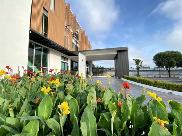 En modern byggnad med en överbyggd entré och en trädgård med gula och röda blommor framför.