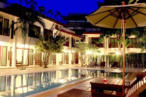 A poolside area with a wooden deck, lounge chairs, and an umbrella.