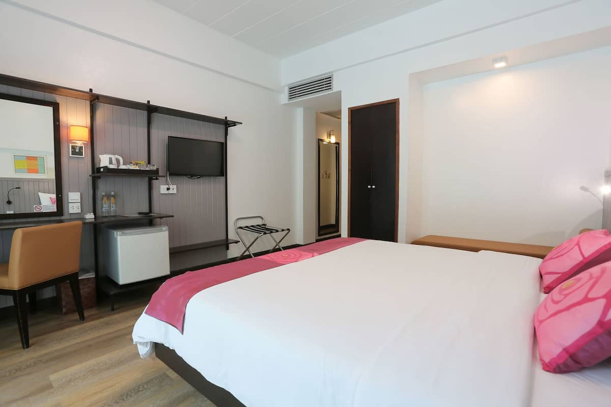 Quarto de hotel com cama, escrivaninha, pequeno espaço de cozinha e espelho.