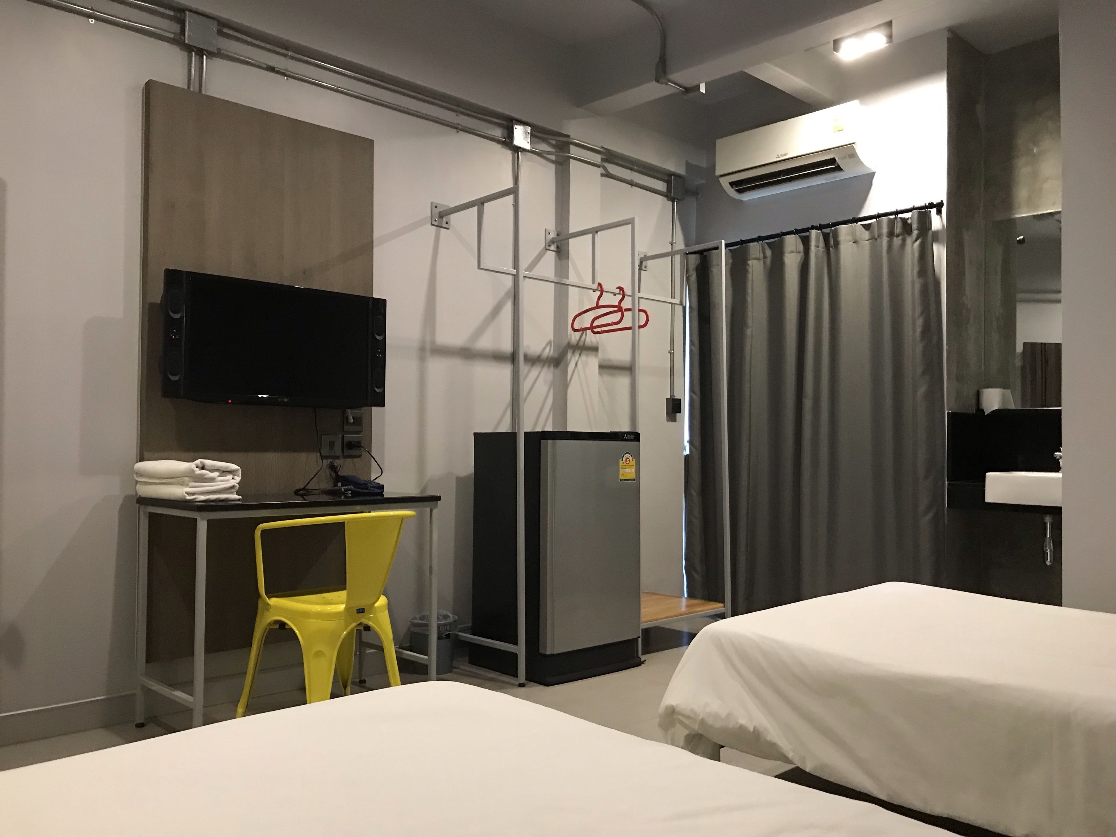 A hotel room with a bed, a desk with a chair, a television, a refrigerator, and a bathroom with a sink and mirror.