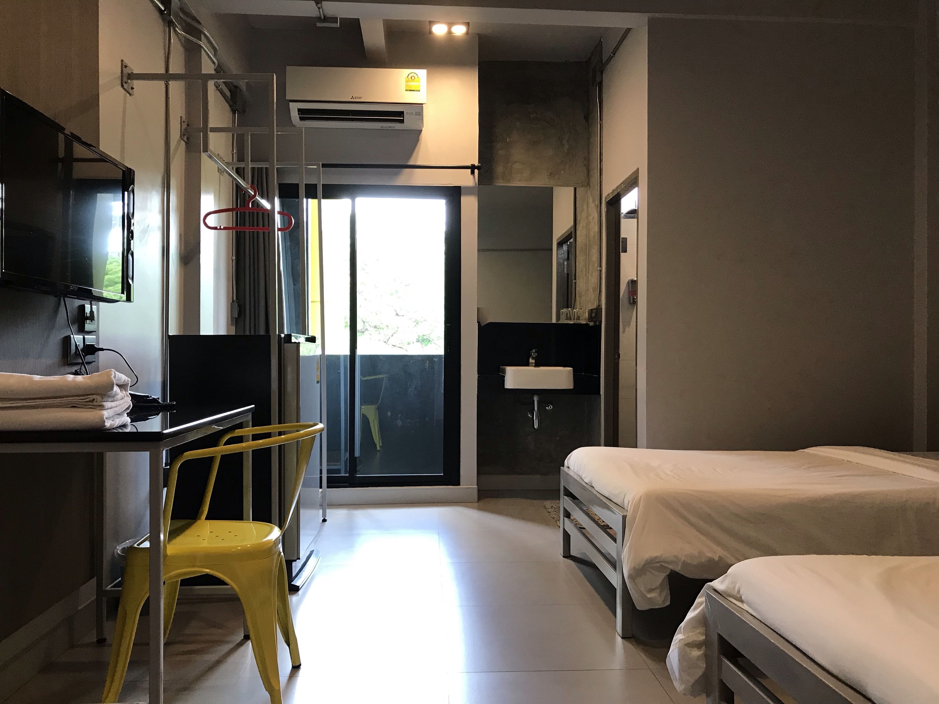 A hotel room with a bed, a desk with a chair, a TV, and a bathroom with a sink.