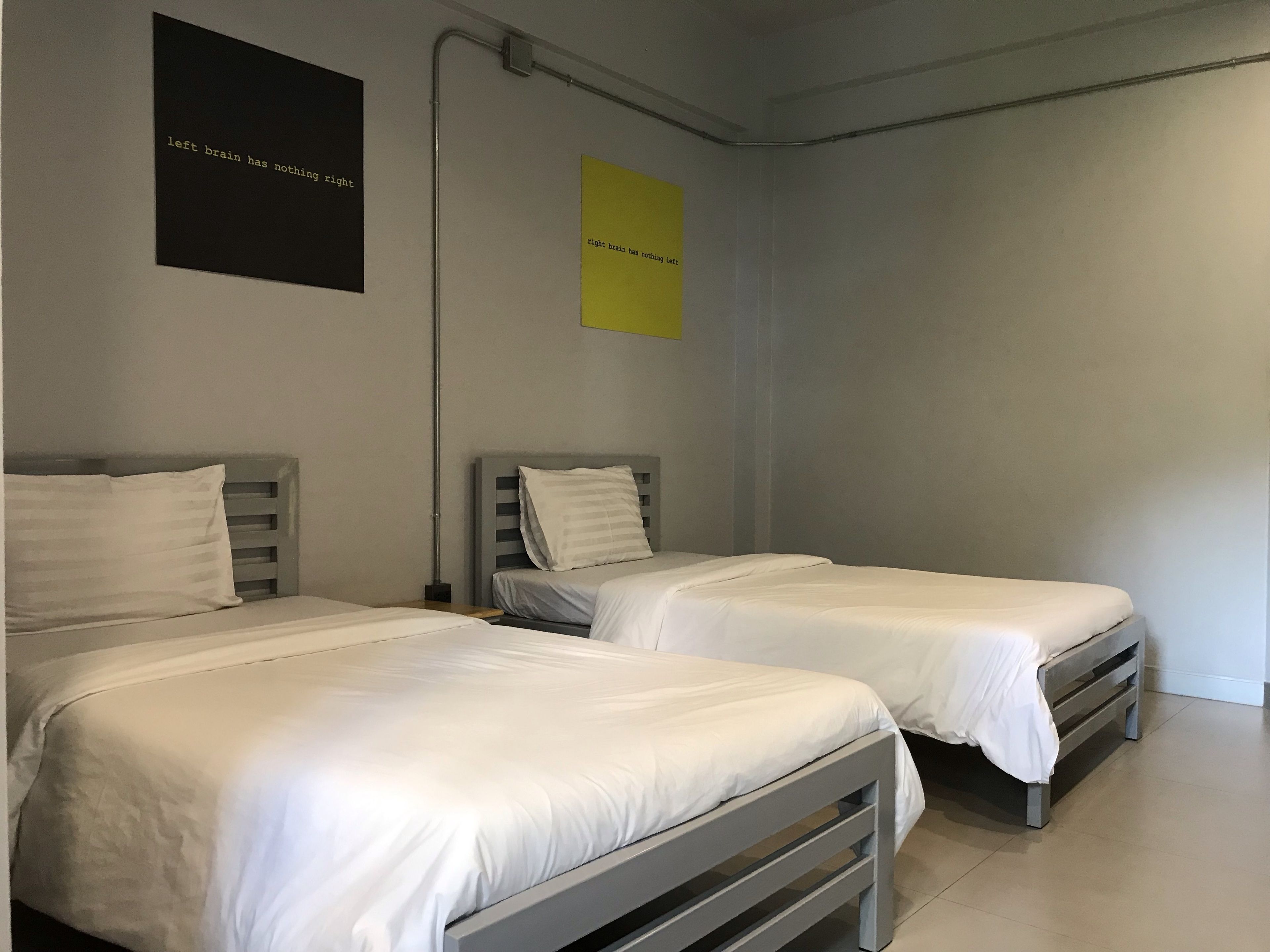 A room with two single beds, each with a grey headboard and white bedding. There are two posters on the wall, one black and one yellow.