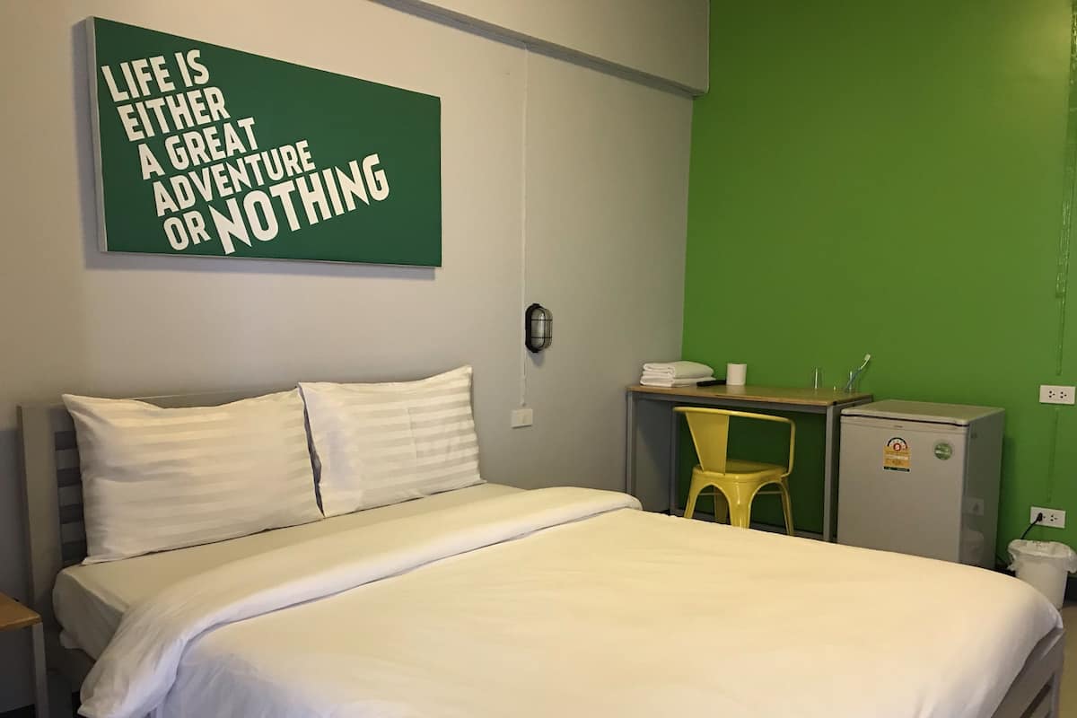 A hotel room with a bed, a desk, a chair, and a small refrigerator.