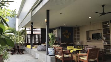 Un espacio de estar al aire libre con mobiliario de madera, una planta en maceta y un televisor en un estante.