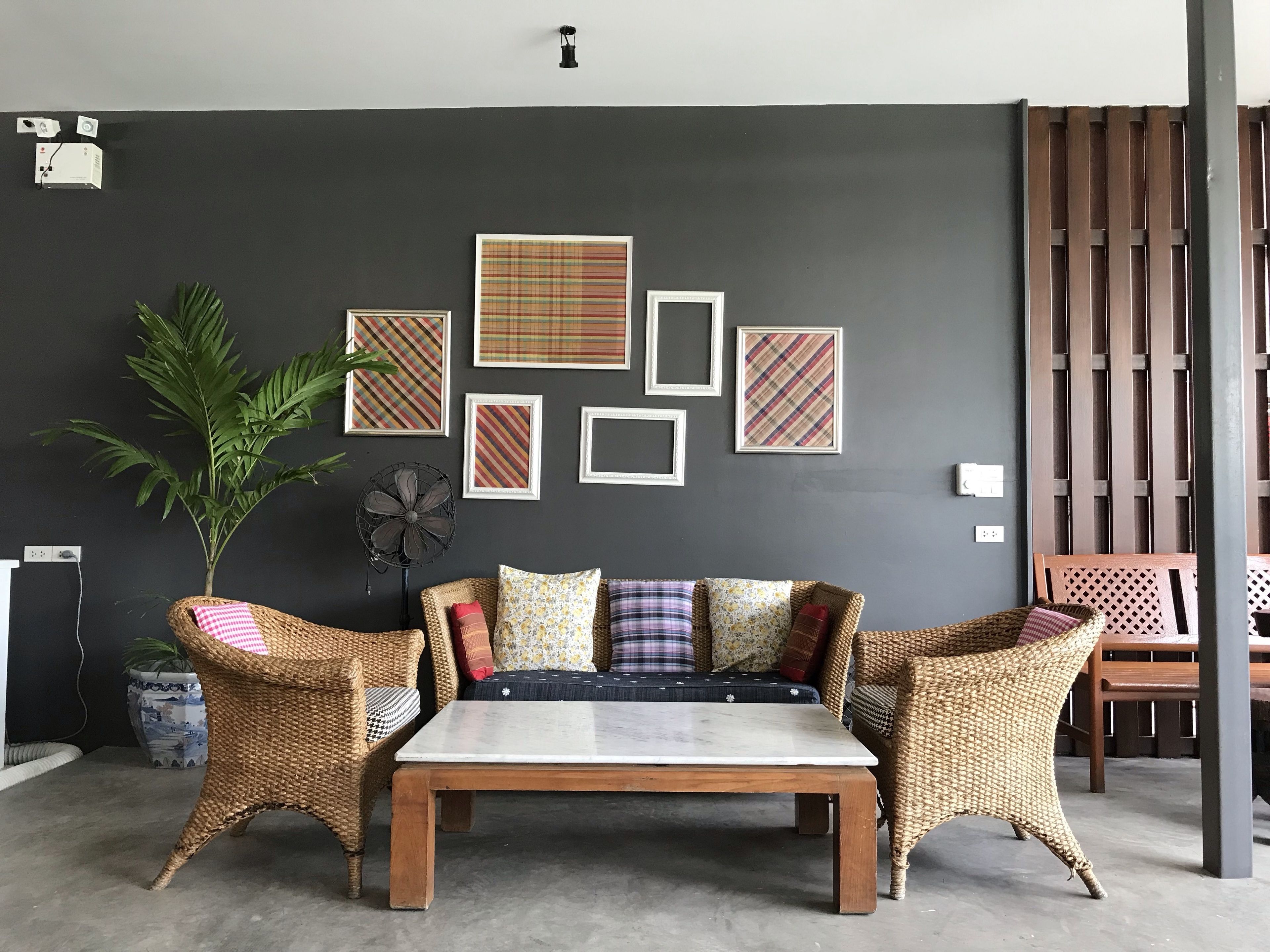 A room with a dark grey wall, a wooden table, wicker chairs, and a sofa with patterned cushions.