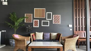 A room with a dark grey wall, a wooden table, wicker chairs, and a sofa with patterned cushions.