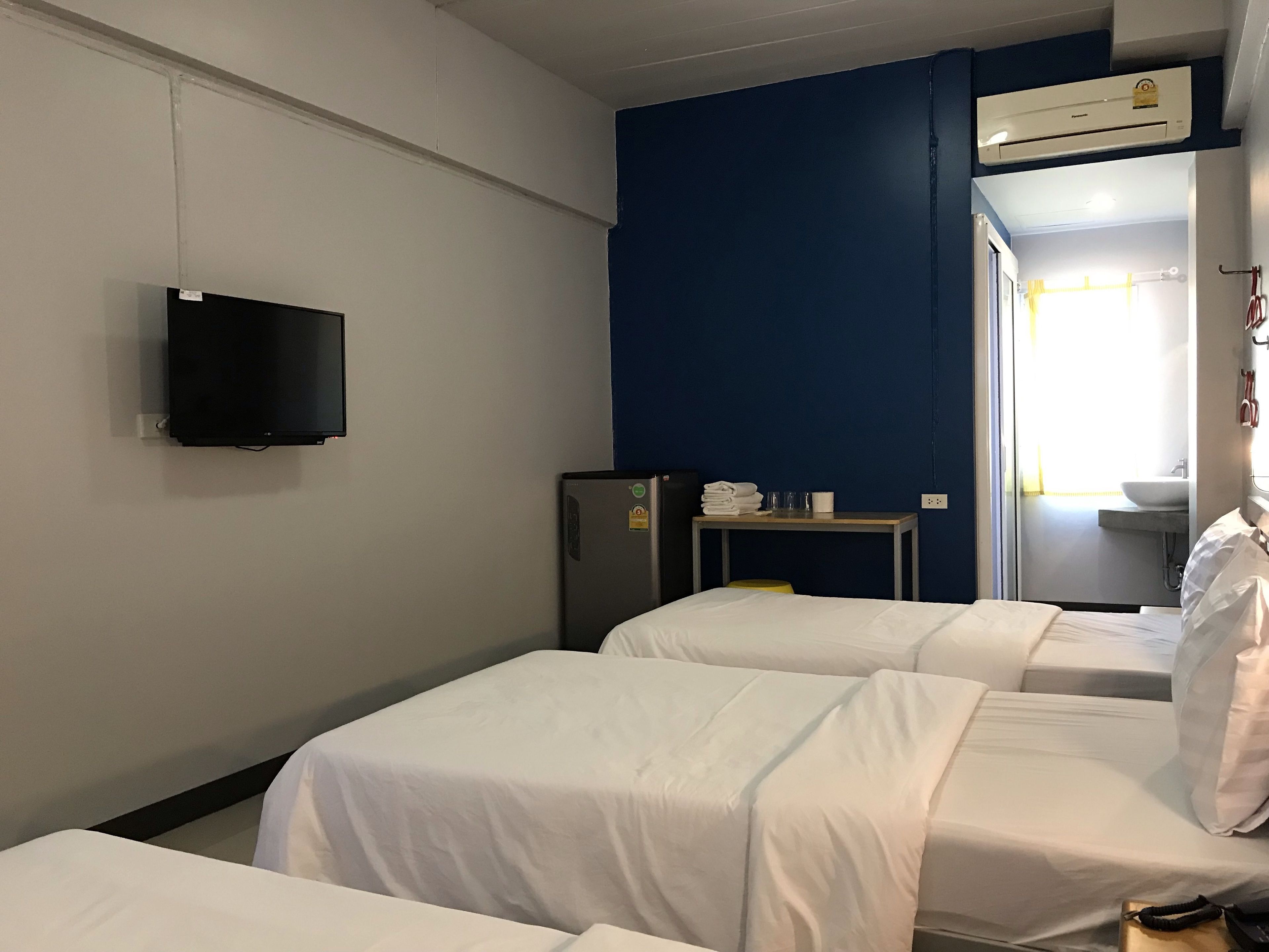 A hotel room with two beds, a television, a small table with towels, a refrigerator, and an air conditioning unit.
