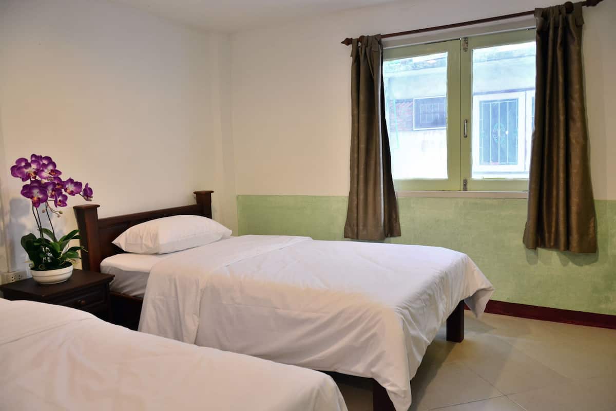 Quarto de hotel com duas camas de solteiro, uma mesinha de cabeceira com planta e uma janela com cortinas.