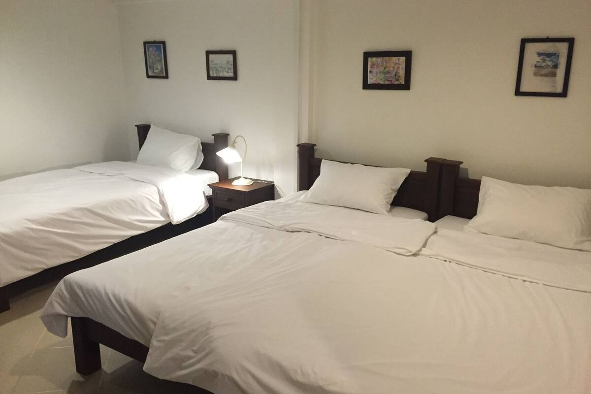 Quarto de hotel com duas camas de solteiro, mesa de cabeceira com abajur e quadros nas paredes.