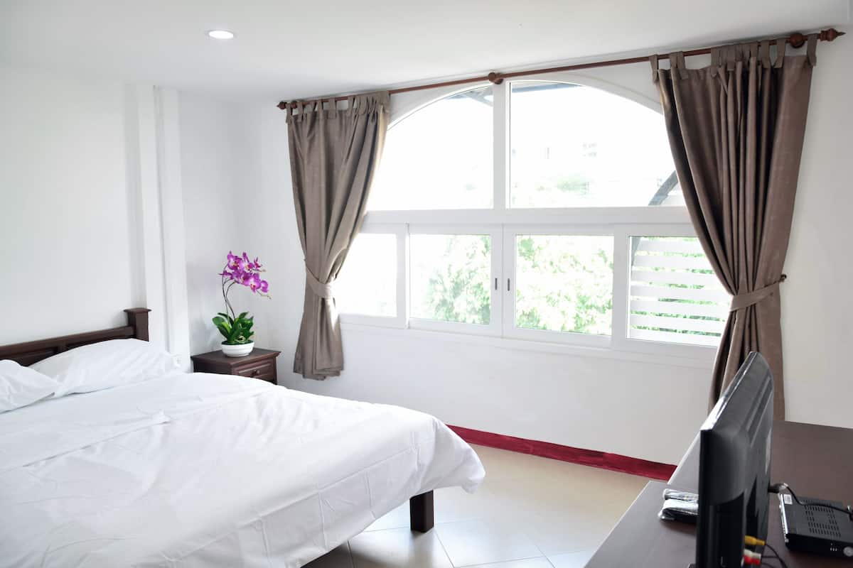 Quarto de hotel com cama, escrivaninha com computador, janela com cortinas e um vaso de planta.