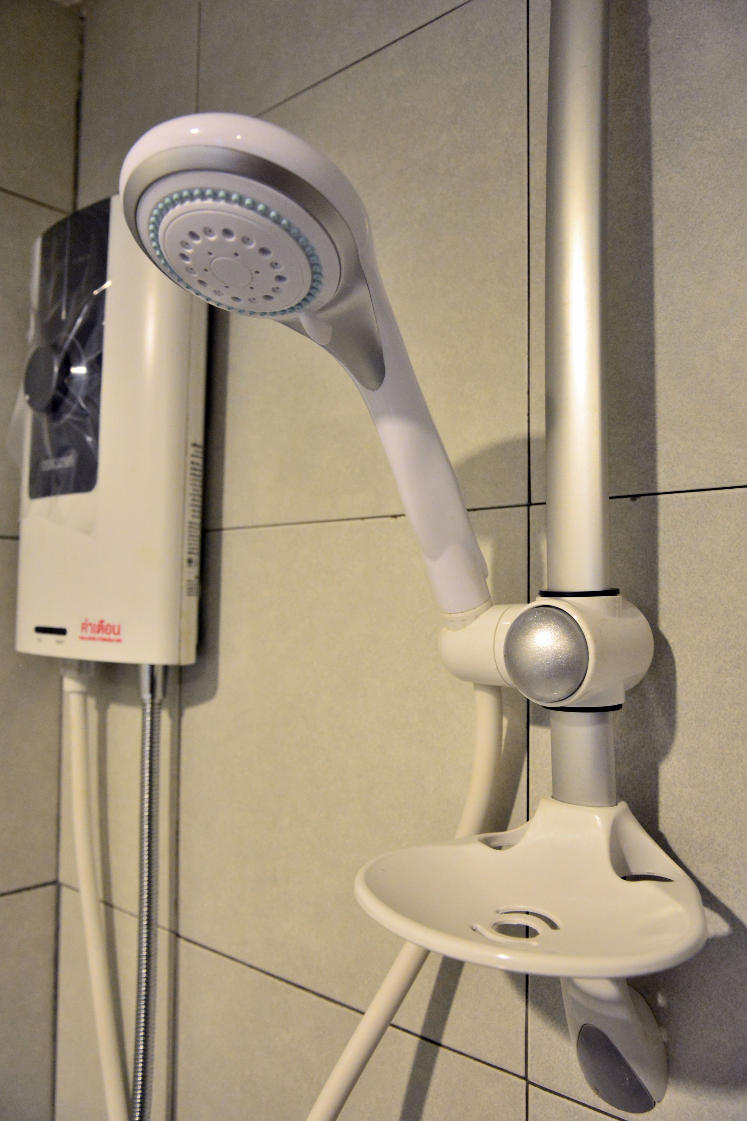 A modern showerhead with a control panel, mounted on a wall with tiled flooring.