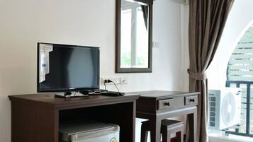 Habitación con televisión, refrigerador pequeño, escritorio, silla, unidad de aire acondicionado y ventana con cortinas.