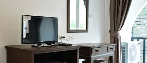 A room with a TV, a small refrigerator, a desk, a chair, an air conditioning unit, and a window with curtains.