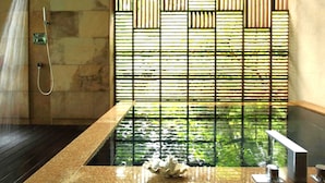 Une salle de bain avec un sol carrelé en pierre, une baignoire, une douche et une fenêtre donnant sur un paysage verdoyant.