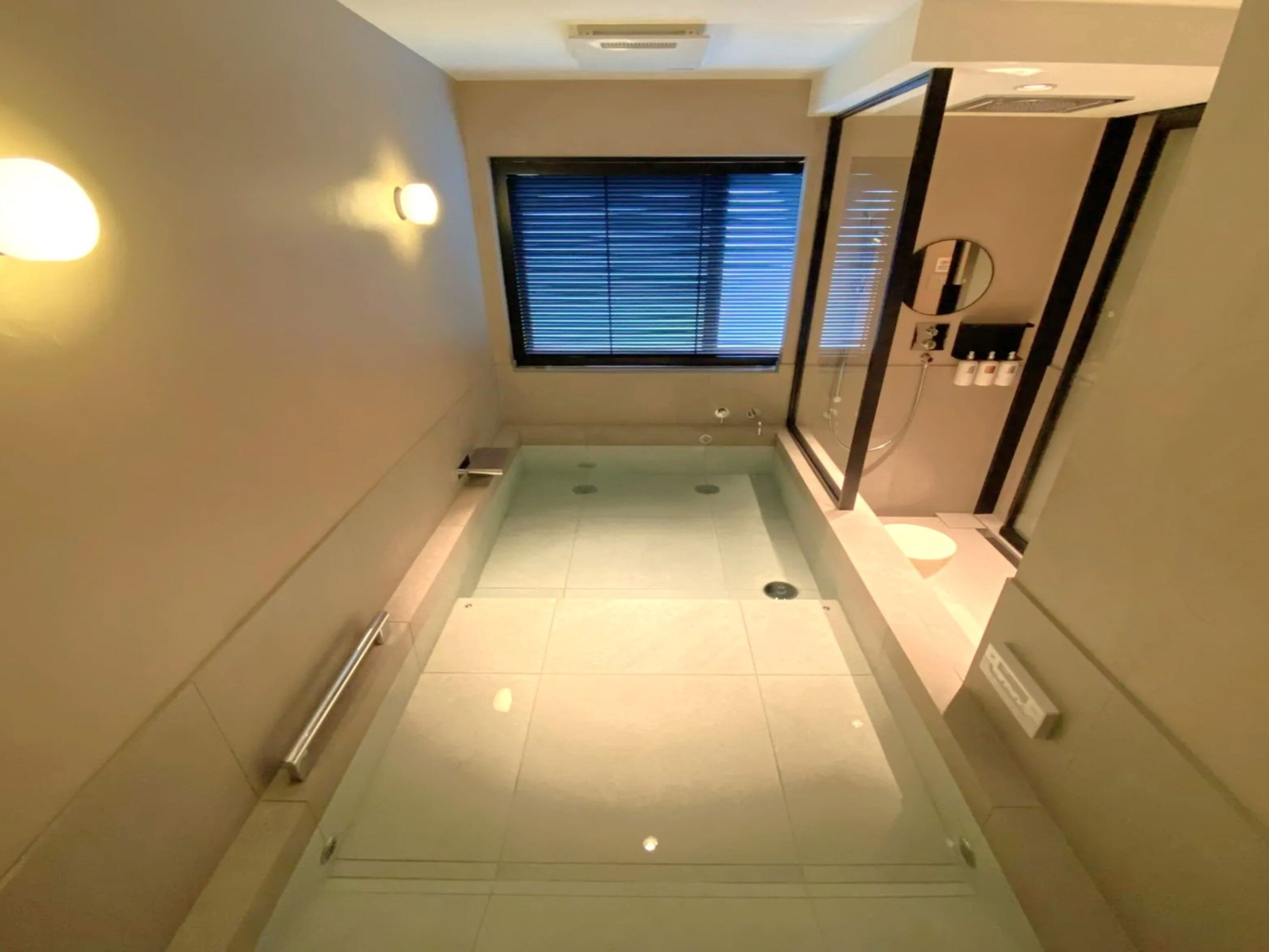 A modern bathroom with a glass shower enclosure, a window with blinds, and a mirror with a towel rack.