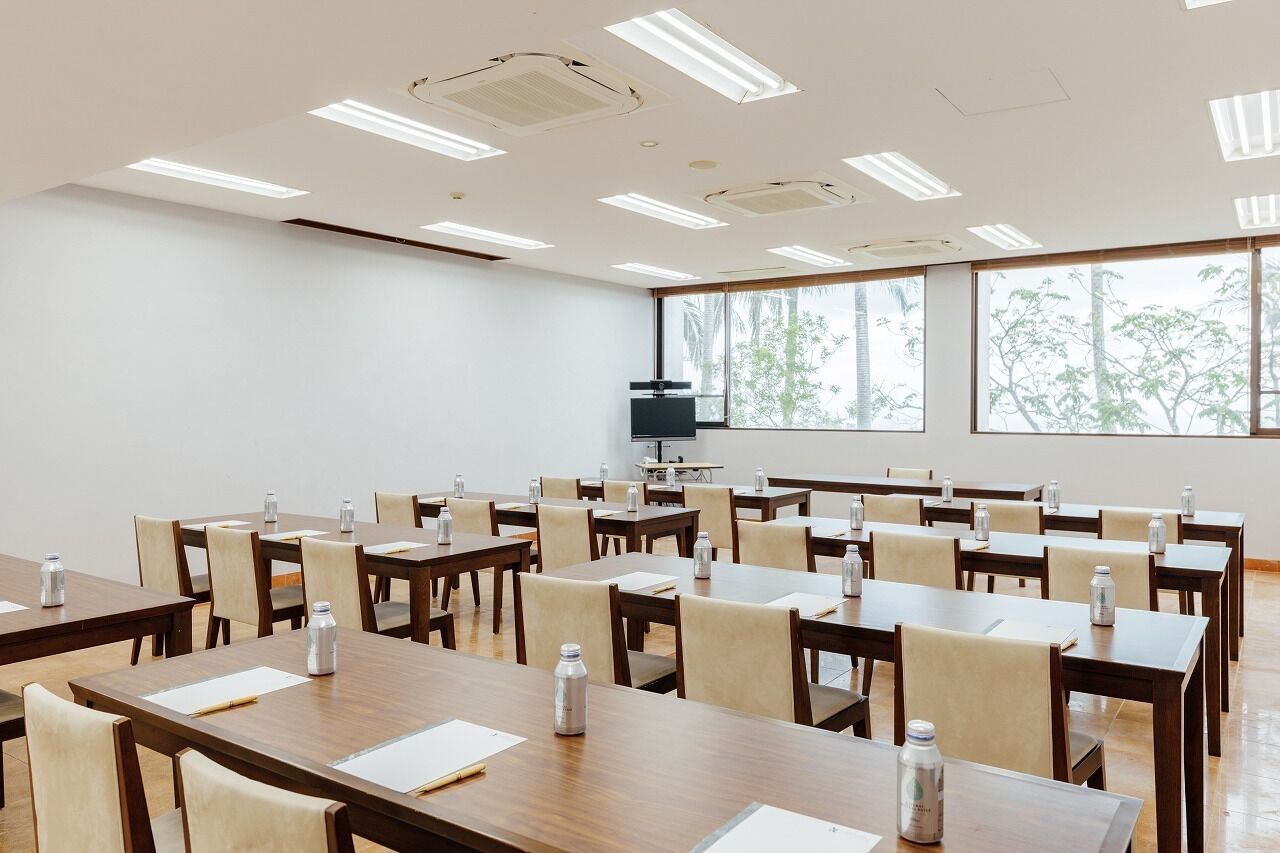 Un salón de conferencias con varias mesas, sillas y una pantalla grande.