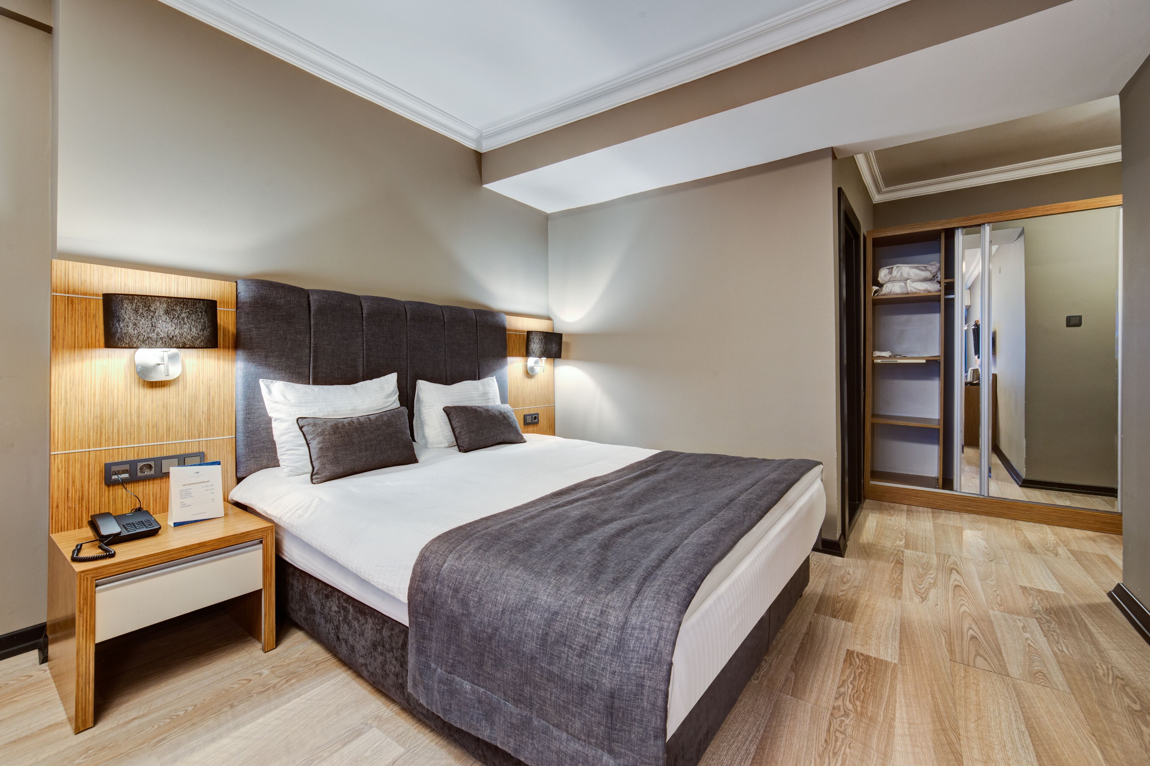 A hotel room with a large bed, bedside tables, a wardrobe, and a mirror.