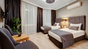 Quarto de hotel com duas camas, televisão, planta e mesa de madeira.