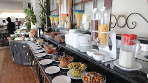 Buffet com diversos alimentos e bebidas, incluindo potes de frutas, oleaginosas e molhos.