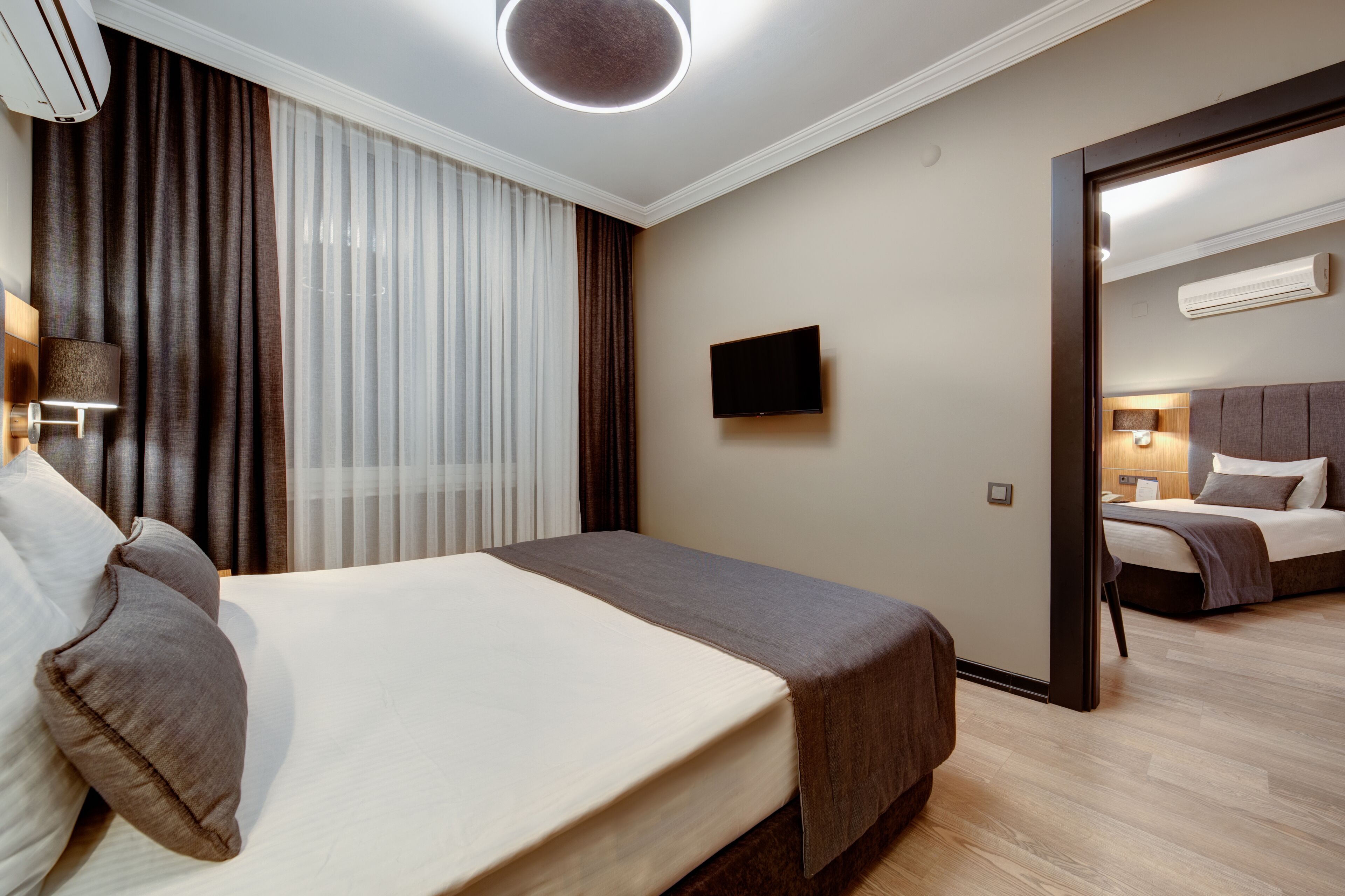 Ein Hotelzimmer mit einem großen Bett, einem Flachbildfernseher, einem Spiegel und Blick auf ein anderes Zimmer.