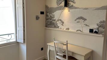 A room with a white desk, a white chair, a wall-mounted light, and a scenic mural.