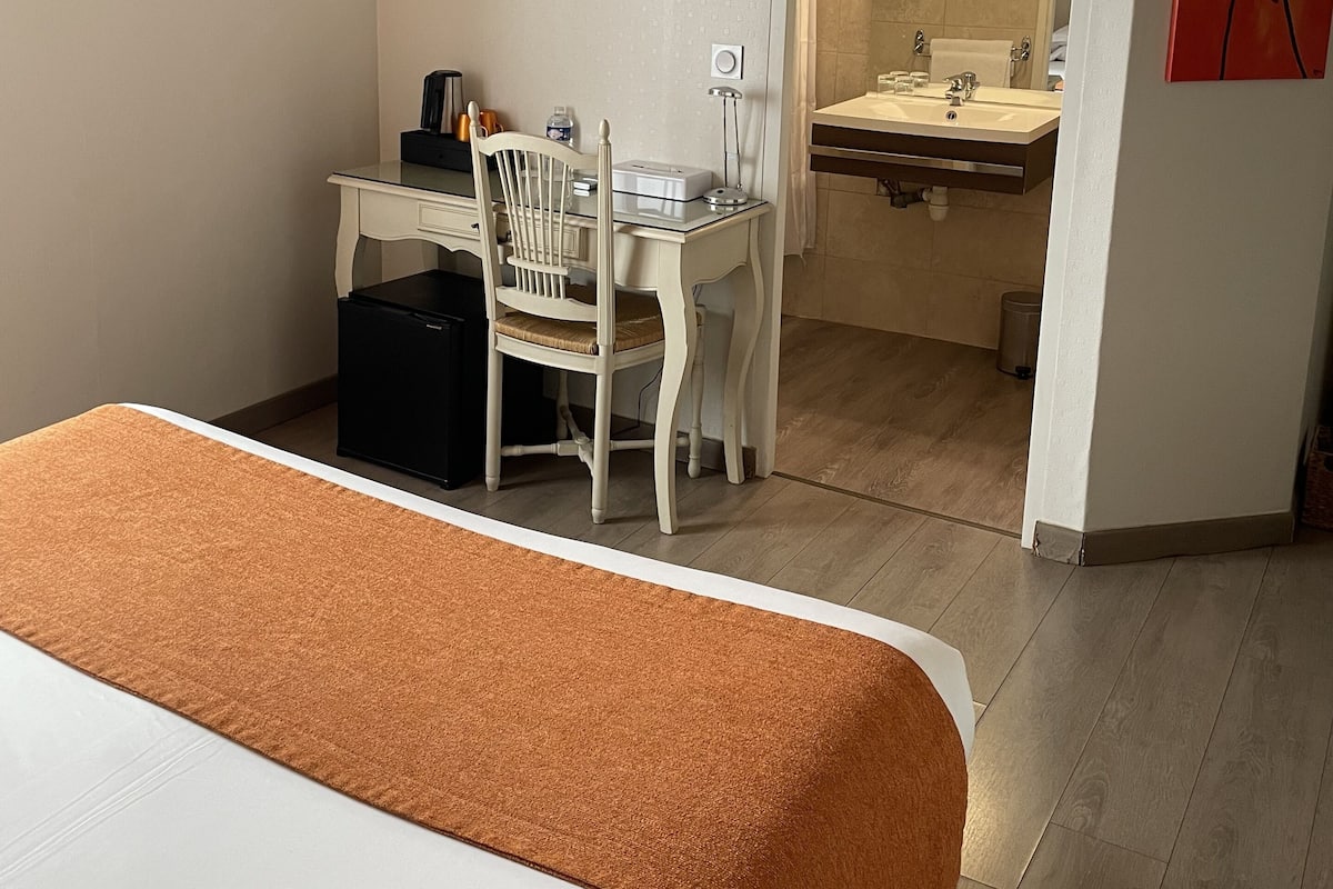 A hotel room with a bed, a desk with a chair, a television, and a bathroom with a sink and mirror.